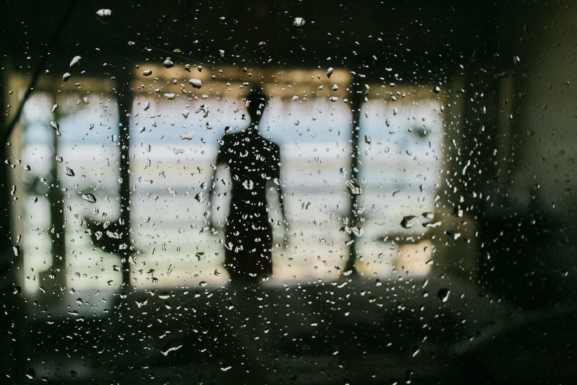 anonymous man behind window in raindrops